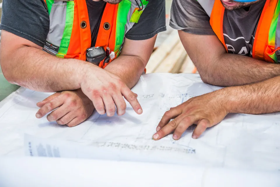 Deux personnes en gilet de chantier relisent un plan sur une table.
